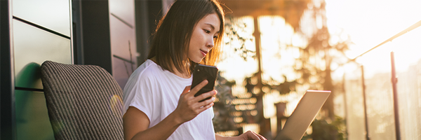 Decorative graphic showing a woman sitting on the porch of her house at sunrise looking at a laptop and holding a cellphone.